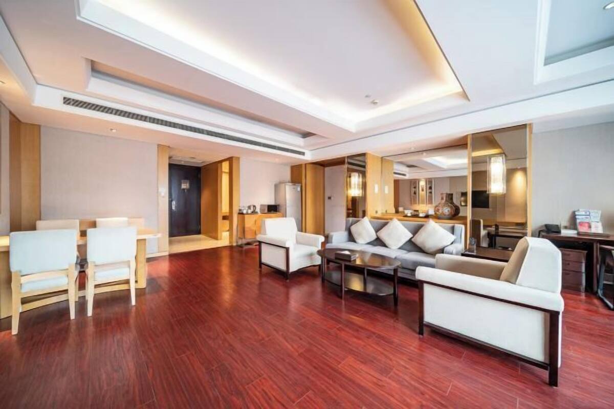A spacious living area with a wooden floor, a sofa set, a coffee table, and a dining area with chairs.