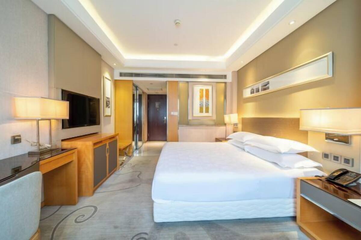A modern hotel room with a large bed, bedside tables, a TV, and a desk.