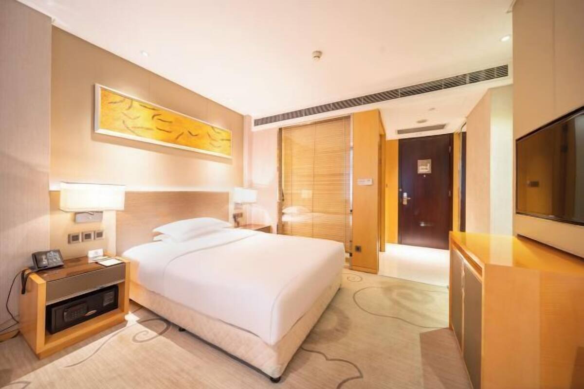 A hotel room with a bed, bedside tables, a TV, and a large window.