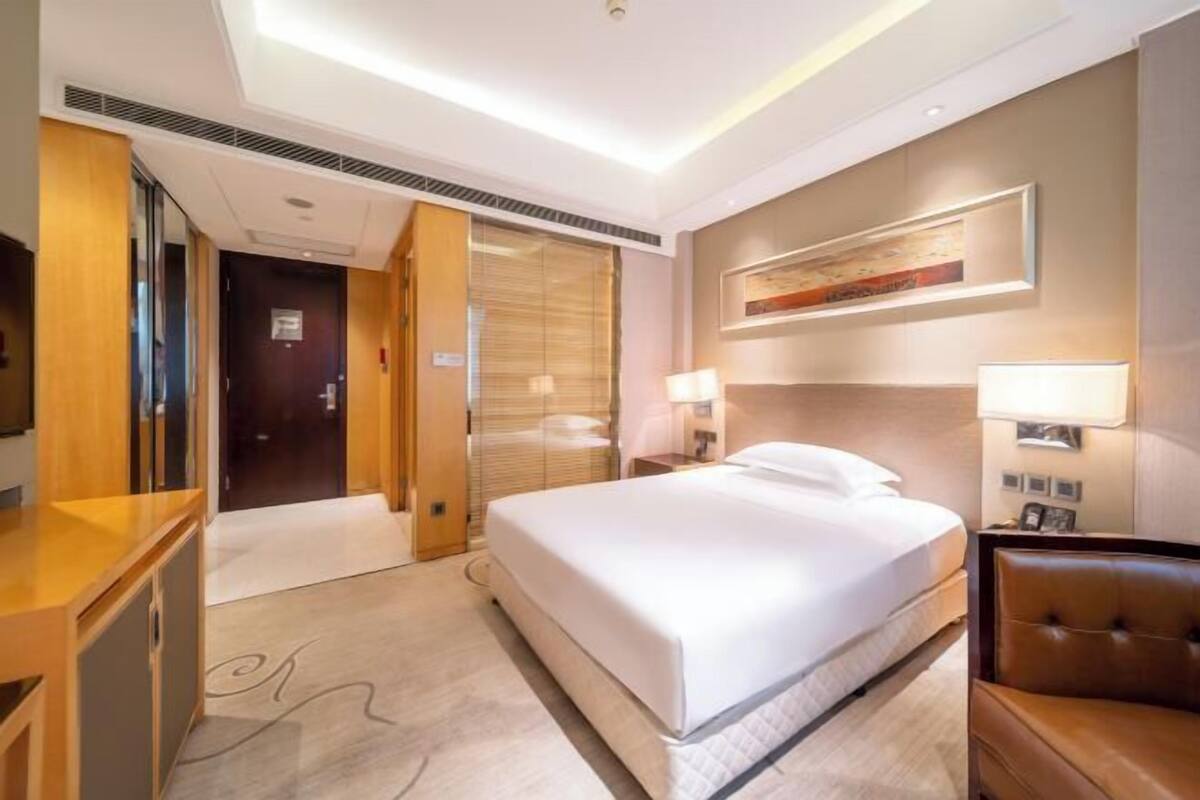 A hotel room with a large bed, a desk, a chair, a TV, and a painting on the wall.