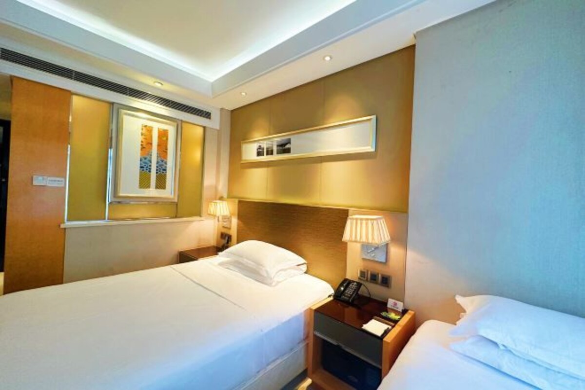 Une chambre d’hôtel avec deux lits, une table de chevet avec une lampe, un téléphone fixé au mur et un tableau encadré au-dessus des lits.
