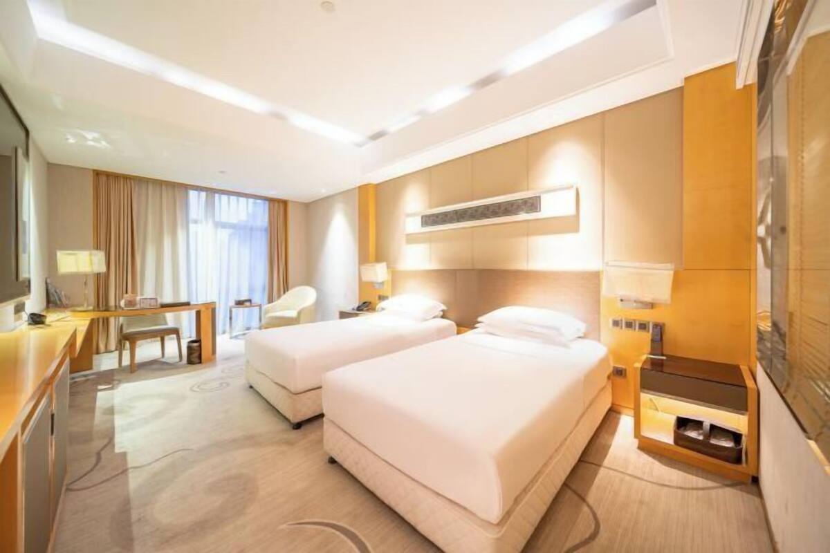A hotel room with two beds, a desk, a chair, a TV, and a minibar.