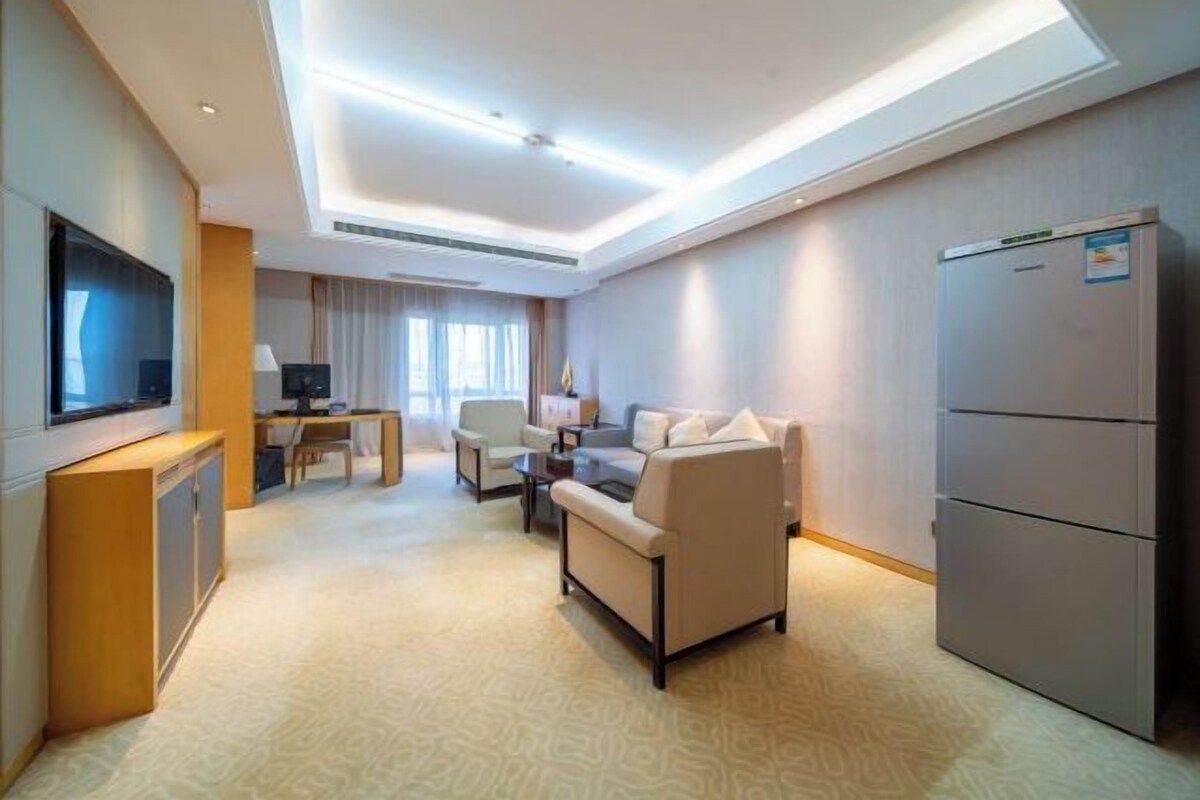 A modern hotel room with a sofa, a TV, a desk, and a refrigerator.