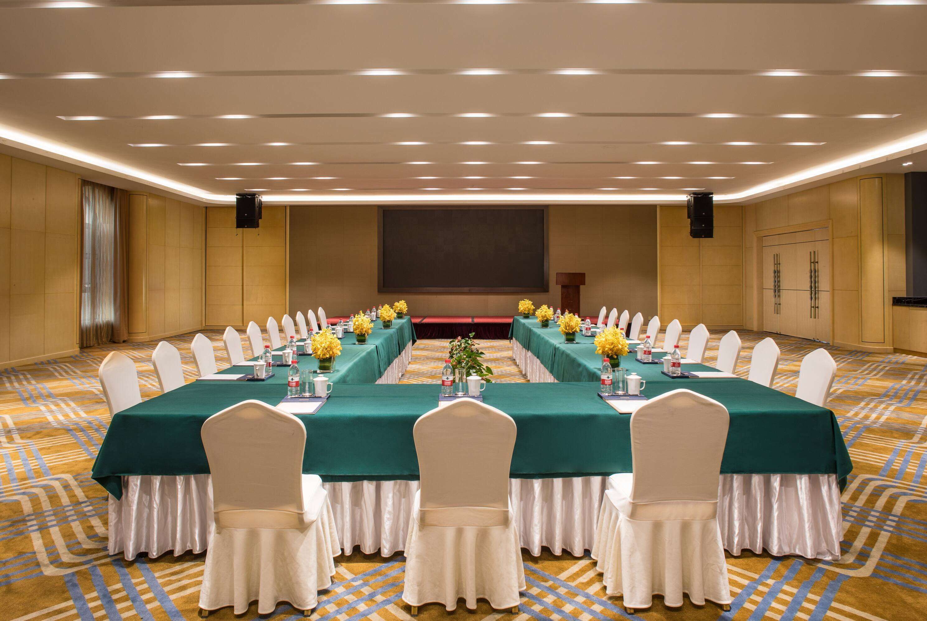 A conference room with a long table, white chairs, and green tablecloths.
