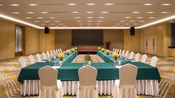 A conference room with a long table, white chairs, and green tablecloths.