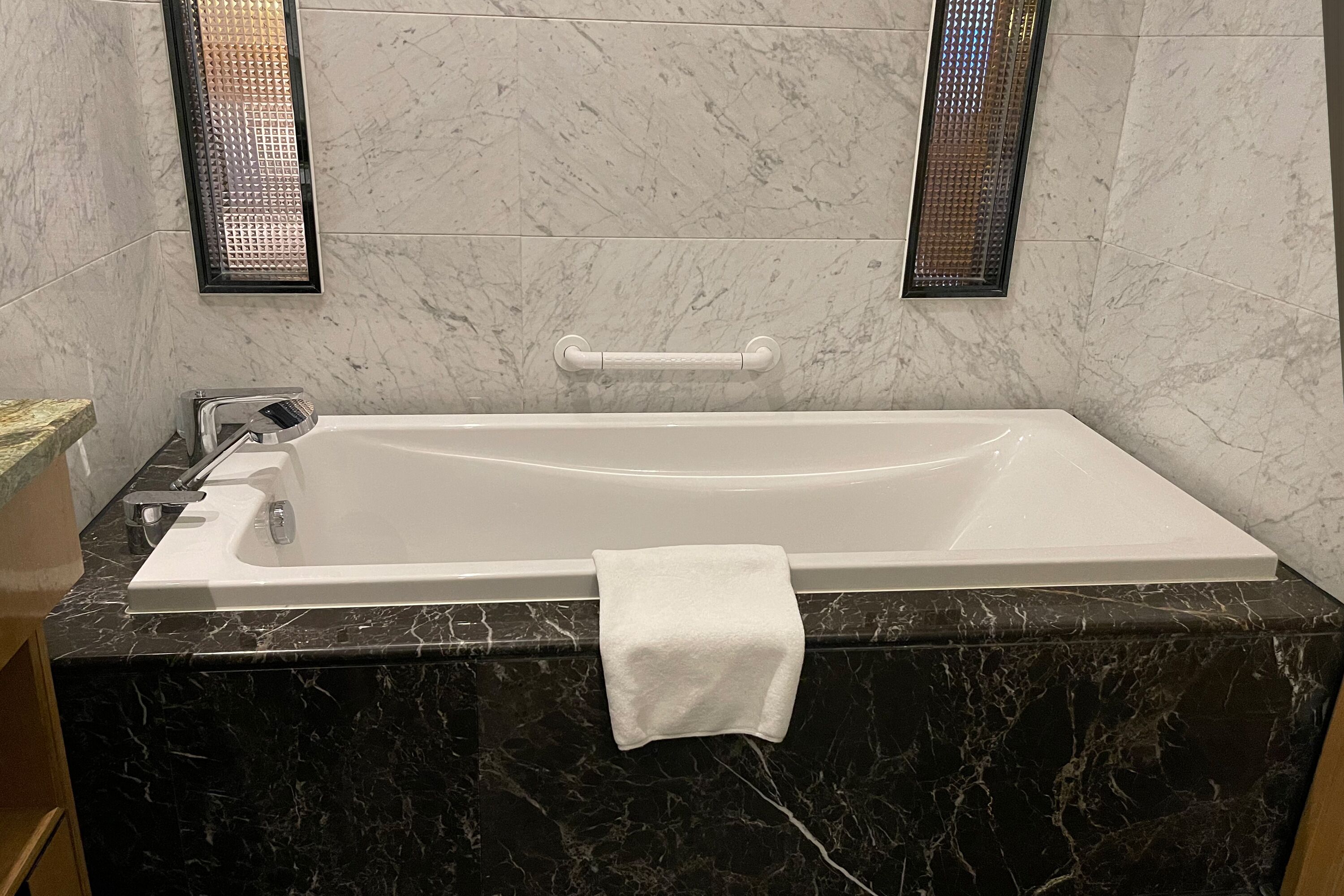 Ein modernes Badezimmer mit einer rechteckigen Badewanne, Marmorwänden und einem Handtuchhalter.