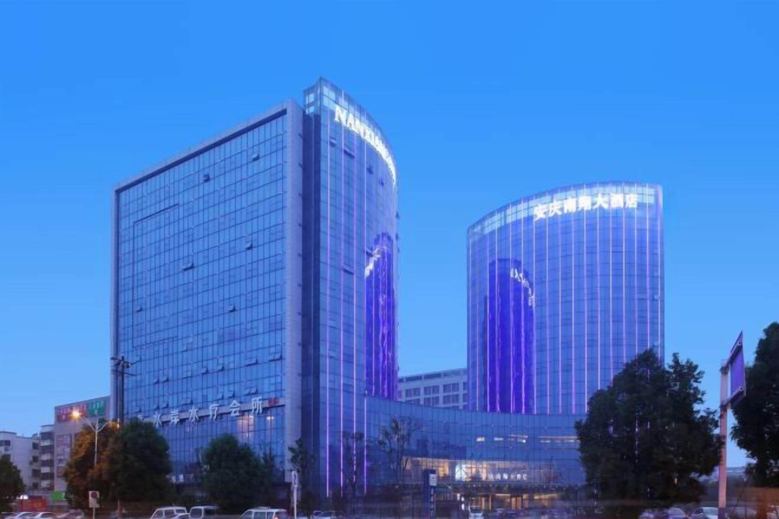 A modern hotel with a glass facade, a prominent entrance, and a large parking area.