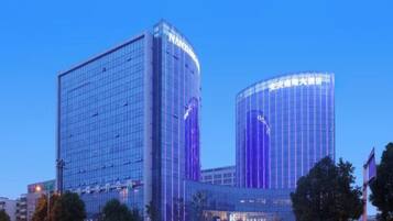 A modern hotel with a glass facade, a prominent entrance, and a large parking area.