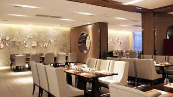 Comedor de hotel con varias mesas y sillas, una pared decorativa con diversos objetos y un espejo grande.