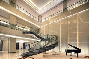 A spacious lobby with a grand staircase, a grand piano, and a high ceiling with modern lighting. - Nanxiang Hotel (Anqing)