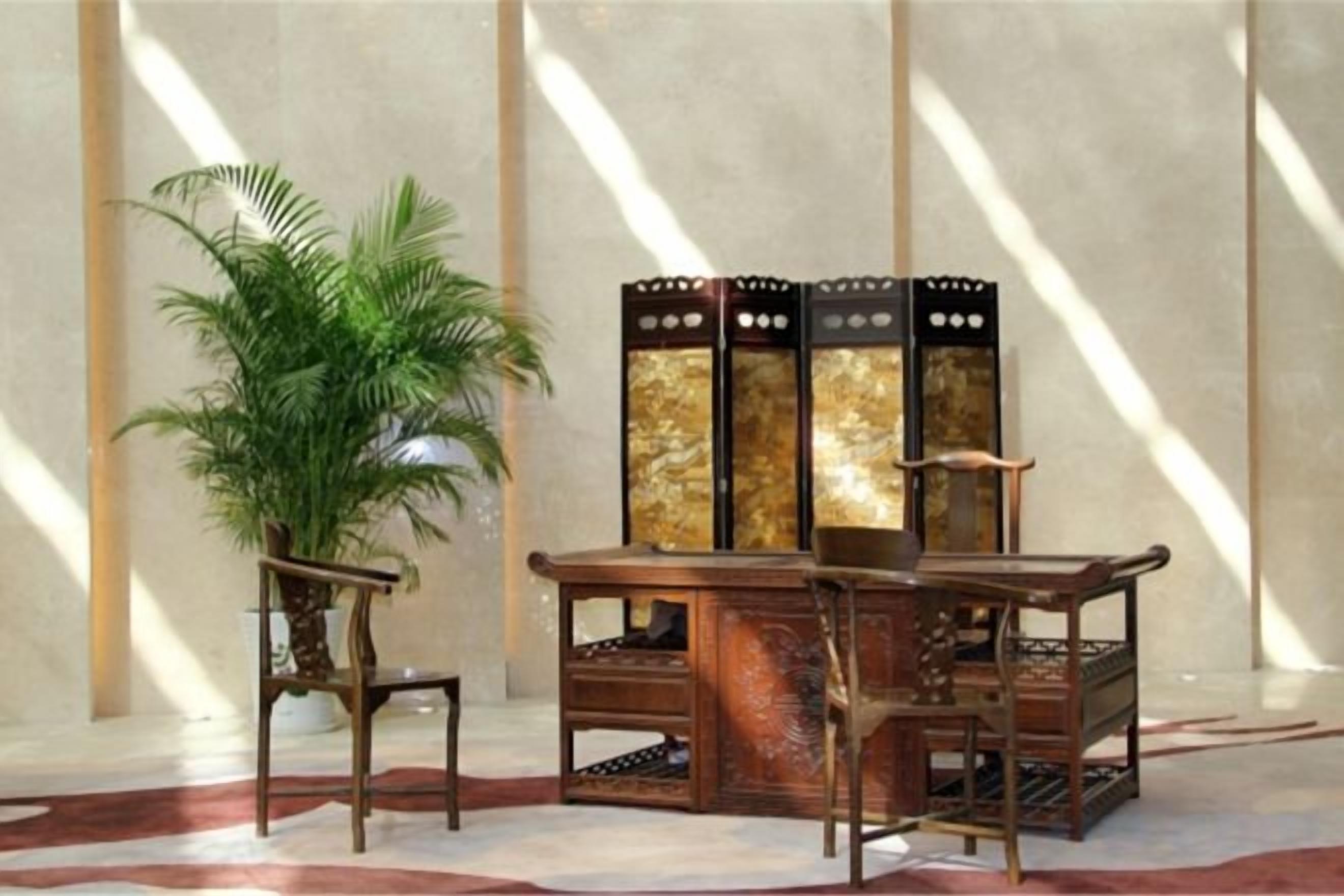 A room with a large potted plant, a wooden cabinet with a decorative top, and a chair.