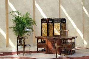 A room with a large potted plant, a wooden cabinet with a decorative top, and a chair. - Nanxiang Hotel (Anqing)