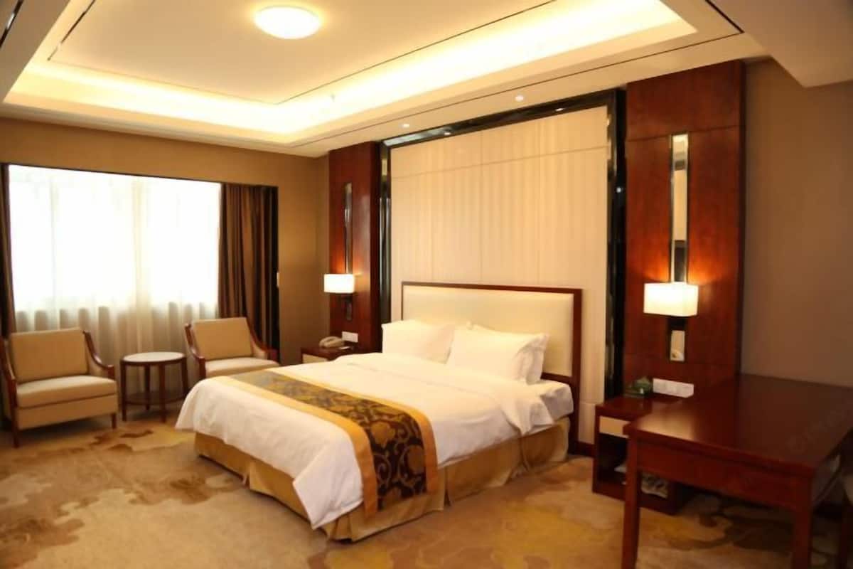 A hotel room with a large bed, a desk, a chair, a small table, and a window with curtains.
