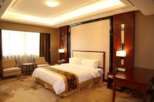 Una habitación de hotel con una cama grande, un escritorio, una silla, una mesita y una ventana con cortinas.