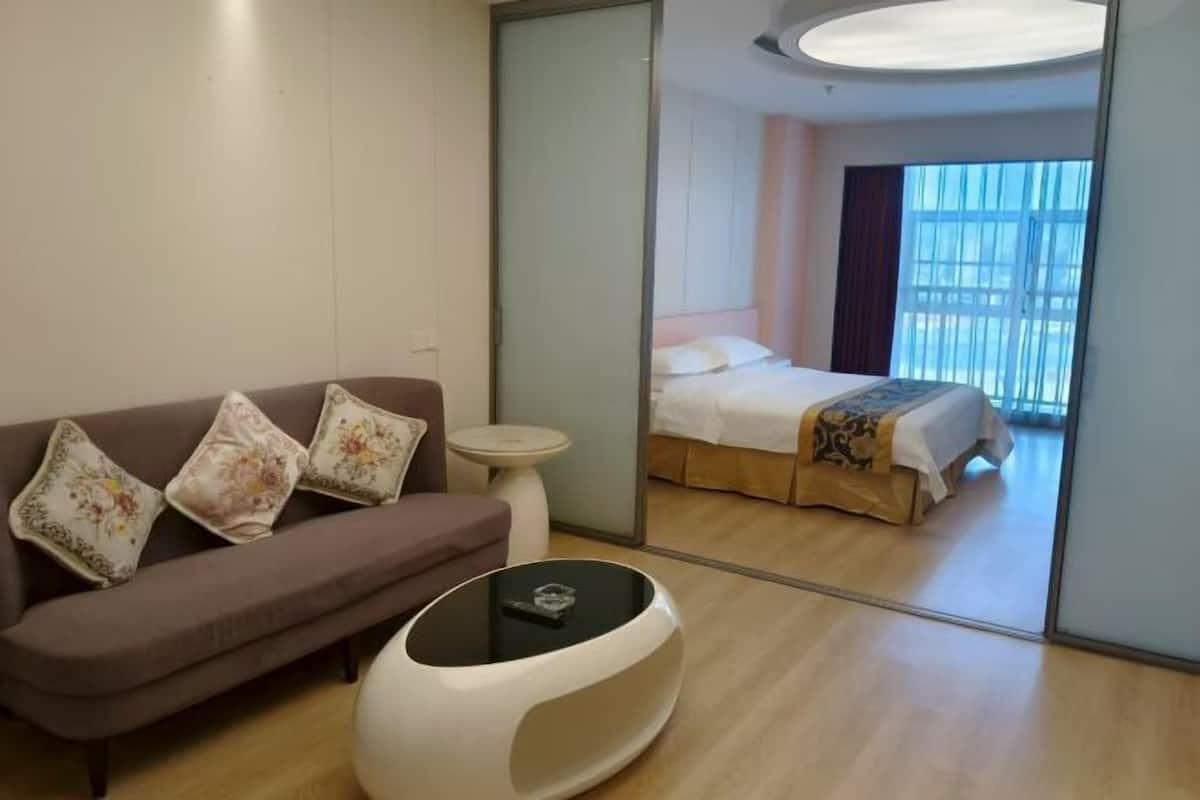 A hotel room with a sofa, a small round table, a bed with a patterned bedspread, and a large mirror reflecting the room.
