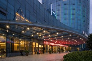 Egy modern hotel, amelynek ívelt üveg homlokzata, feltűnő piros felirata és jól megvilágított bejárati területe van.