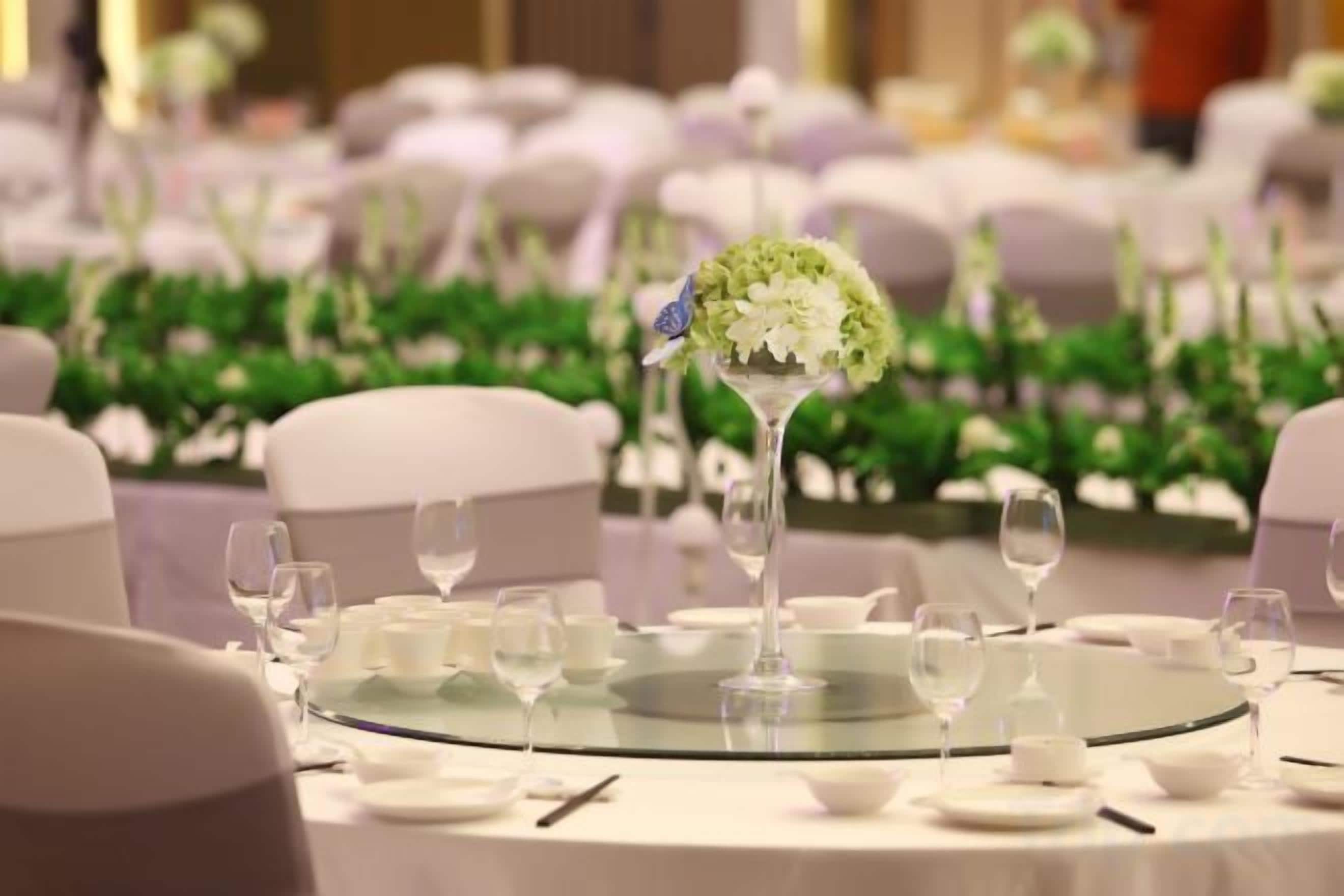 A round table with a glass top, surrounded by white chairs and set with plates, glasses, and cutlery.
