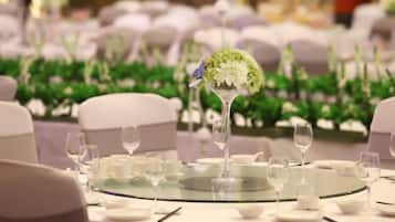 A round table with a glass top, surrounded by white chairs and set with plates, glasses, and cutlery.