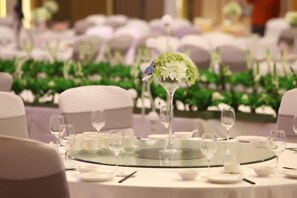 A round table with a glass top, surrounded by white chairs and set with plates, glasses, and cutlery. - Nanxiang Hotel (Anqing)