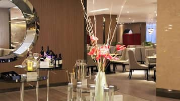 A hotel lobby with a round mirror, a glass table with a vase of flowers, and a bar area with bottles.