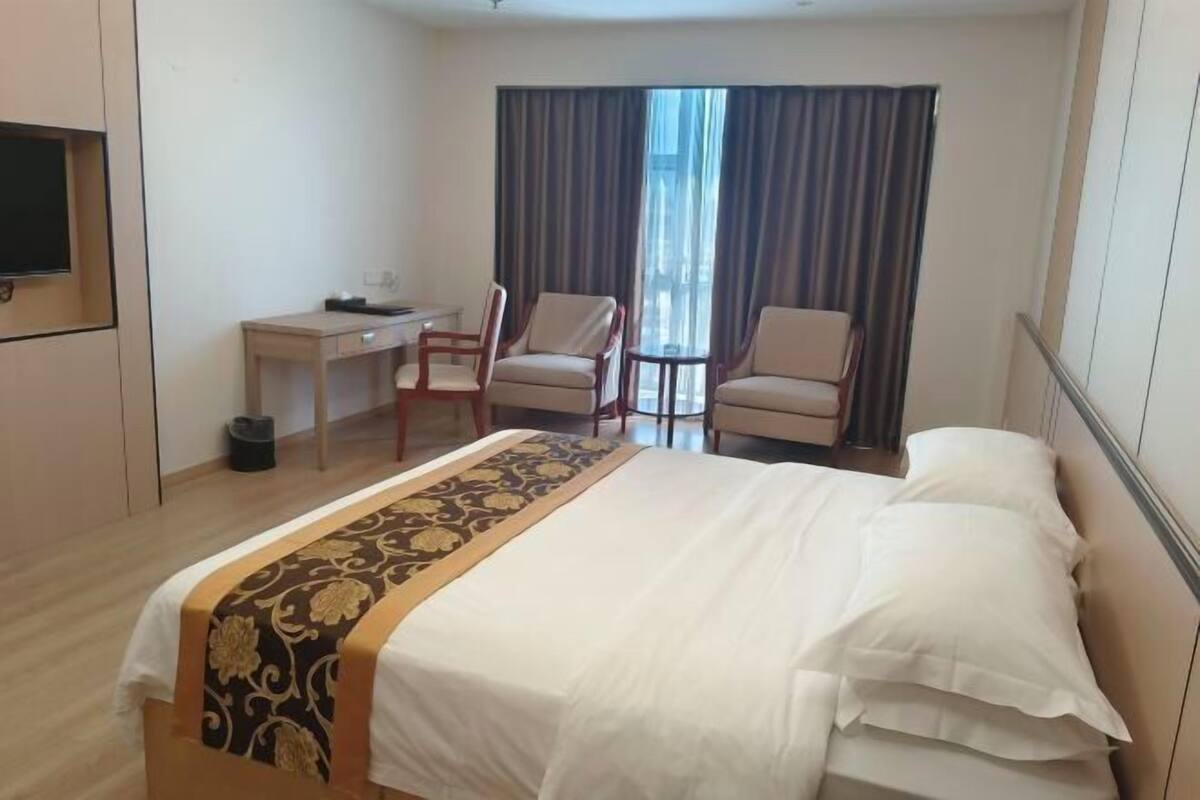 A hotel room with a bed, a desk, two chairs, a television, and a window with curtains.