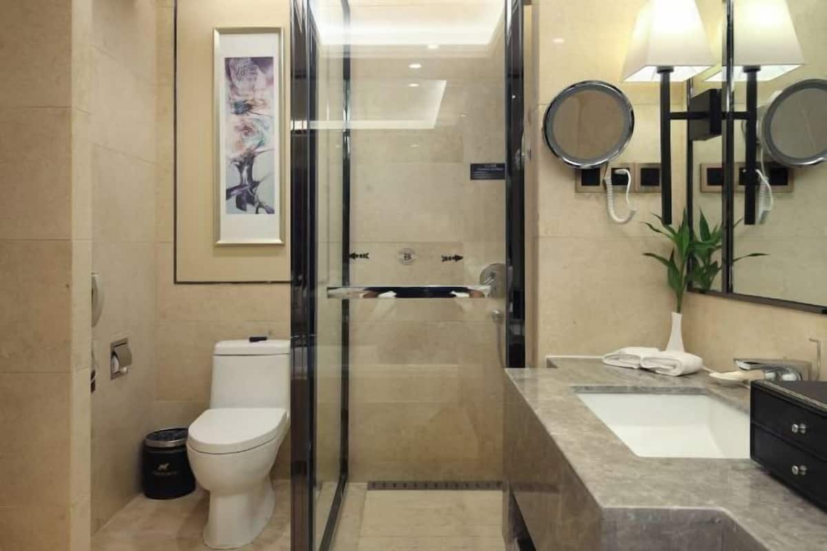 A modern bathroom with a glass-enclosed shower, a toilet, a sink with a mirror, and a framed artwork on the wall.