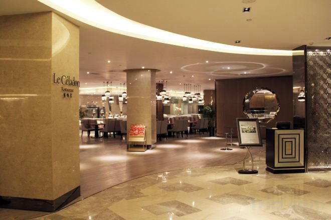 A hotel lobby with a curved marble floor, a reception desk, and a dining area in the background.