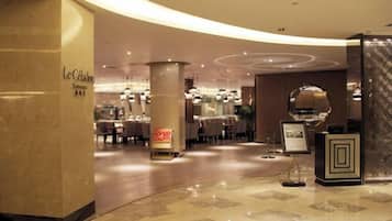 A hotel lobby with a curved marble floor, a reception desk, and a dining area in the background.