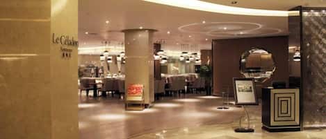 Un vestíbulo de hotel con suelo de mármol curvo, un mostrador de recepción y un comedor al fondo.