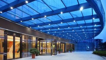 Una entrada de hotel moderna con fachada de vidrio, una galería techada y plantas en macetas.