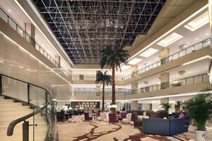 A multi-level hotel lobby with a central atrium, palm trees, and seating areas.