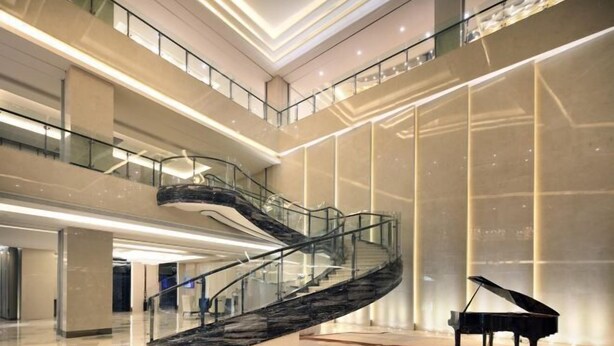 A modern interior with a curved glass staircase, a grand piano, and a spacious atrium with high ceilings and natural light. - Nanxiang Hotel (Anqing)