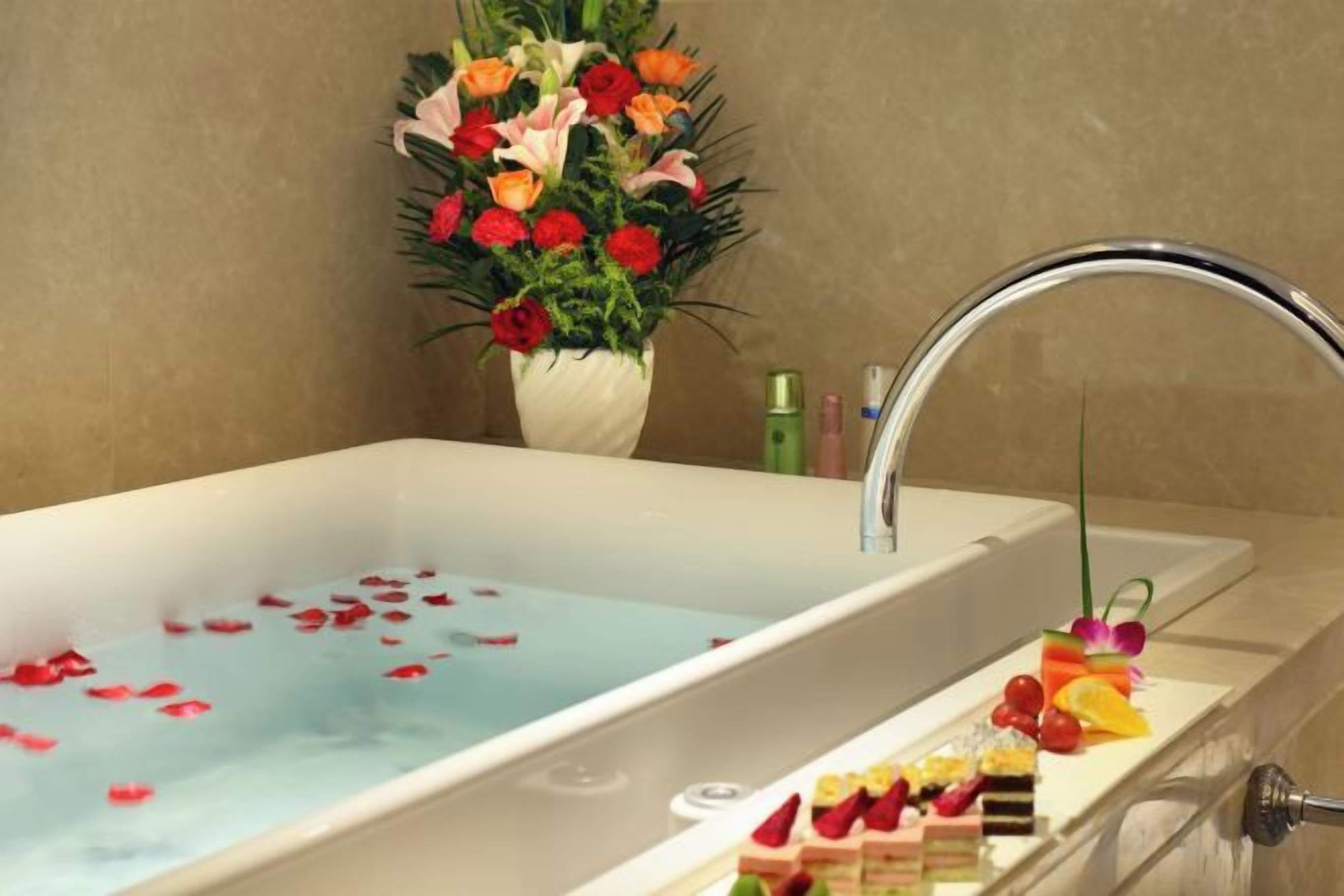 Une baignoire remplie de pétales de roses, un bouquet de fleurs et un plateau de fruits.