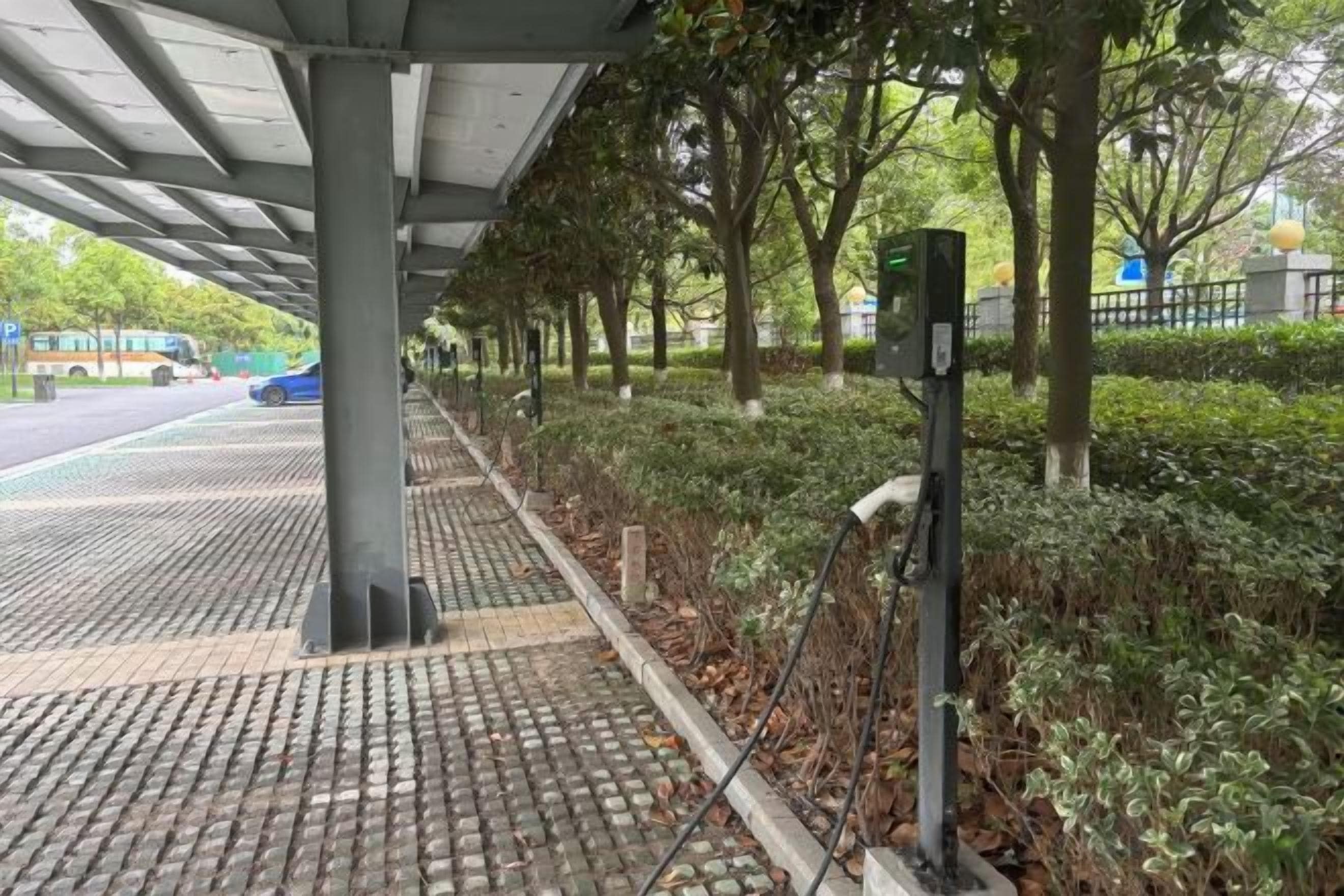 A covered pedestrian walkway with a metal structure, trees, and a road in the background.