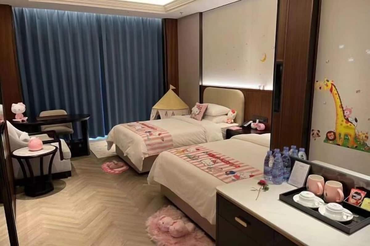 Ein Hotelzimmer mit zwei Betten, einem Schreibtisch, einem Stuhl, einer Lampe und einer Wand mit Giraffendekoration.