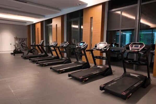 Une rangée de tapis de course dans une salle de sport dotée de grandes fenêtres et d’un design moderne.