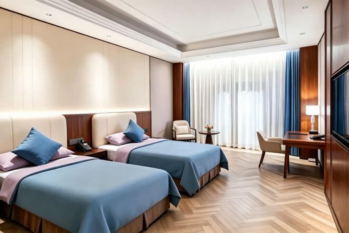 Una camera d'albergo con due letti, una scrivania, una sedia, una televisione e una finestra con tende.