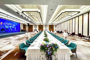 Un salón de conferencias con una mesa larga, sillas y un escenario con una pantalla.