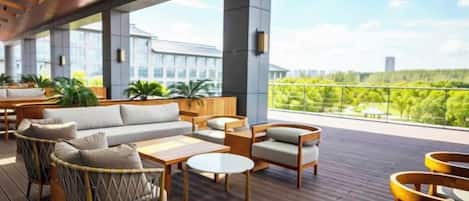 A spacious outdoor seating area with wooden furniture and a view of greenery.