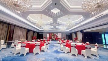 Un amplio salón de conferencias con mesas redondas y sillas blancas, candelabros y alfombra azul.