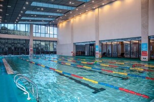 Una piscina interior con varias pistas de natación, un trampolín y una amplia zona con ventanas.