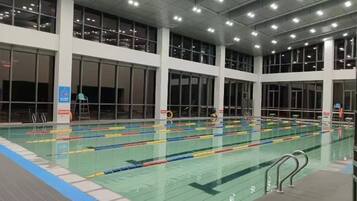 Piscina interna com várias pistas de natação, amplas janelas e piso revestido de azulejos.