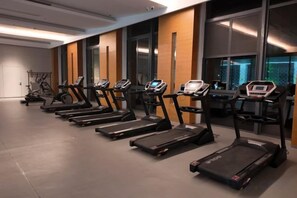 A row of treadmills in a gym with large windows and a door in the background. - Yancheng Guest Hotel (Yancheng City)