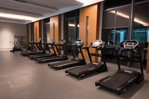 Varias caminadoras en un gimnasio con ventanas amplias y una puerta al fondo.