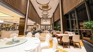 Eine moderne Hotelhalle mit einer zentralen Wendeltreppe, verschiedenen Gastronomiebereichen und einem großen Fenster für natürliches Licht.