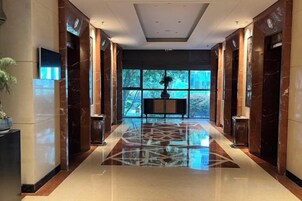 Un vestíbulo de hotel con un largo pasillo, suelo de mármol y grandes ventanales.
