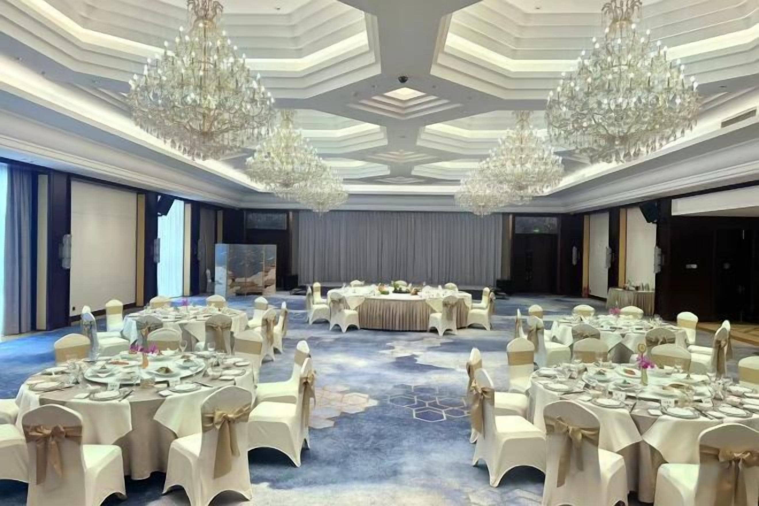 Un salón de banquetes con mesas redondas, sillas blancas y candelabros.