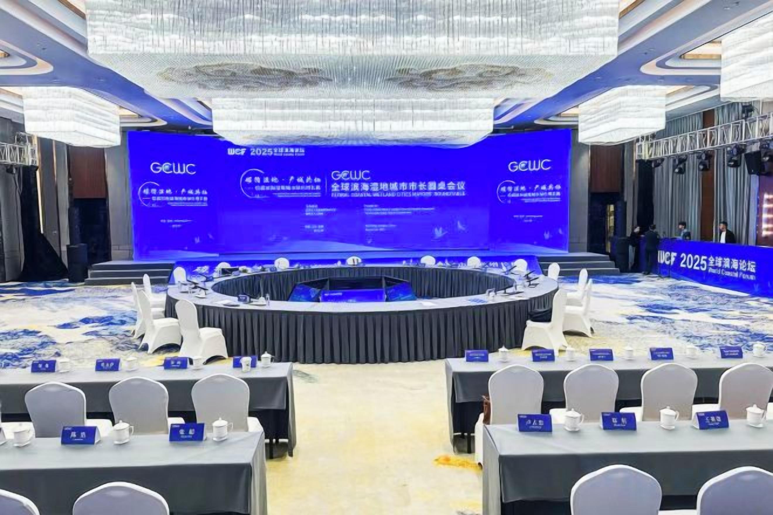 A conference room with a round table, chairs, and a stage with a blue backdrop.