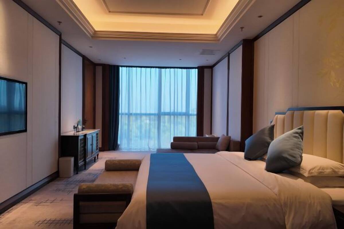 Ein modernes Hotelzimmer mit einem großen Bett, einem Fernseher, einer Sitzecke und Blick aus dem Fenster.