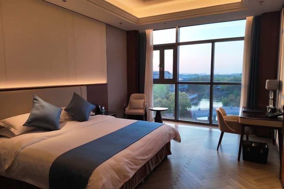 Ein Hotelzimmer mit einem großen Bett, einem Schreibtisch, einem Stuhl und Blick auf einen Fluss.